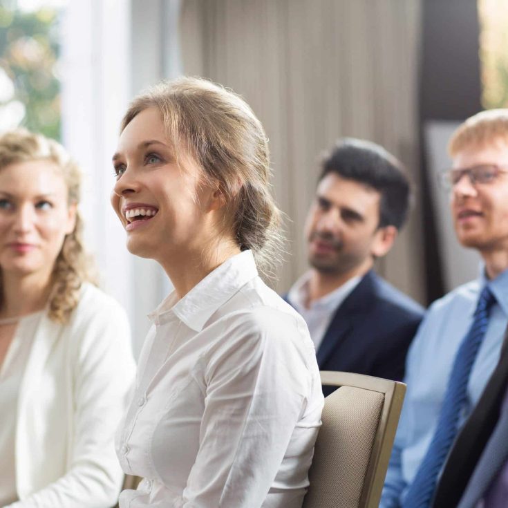 Young businesswoman and her male and female colleagues smiling, sitting and watching presentation in conference room