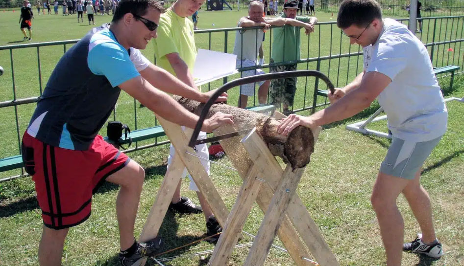 Mladý muži spoločne pília kus dreva. Vhodná aktivita pre teambuilding.