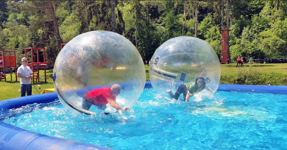 Muž a žena v priesvitnej guli prechádzajúci sa po vode. Vhodná aktivita pre teambuilding.